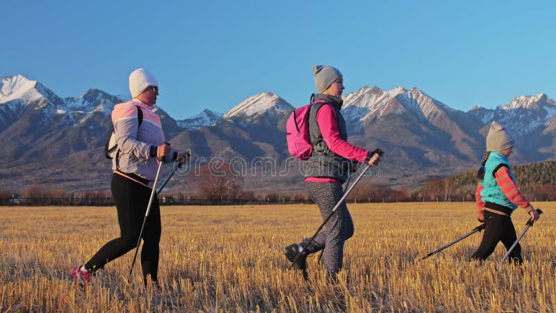 Vrouw loopt noords in de natuur op de achtergrond van bergen in het veld Meisjes en kinderen gebruiken trekstokken en noordse