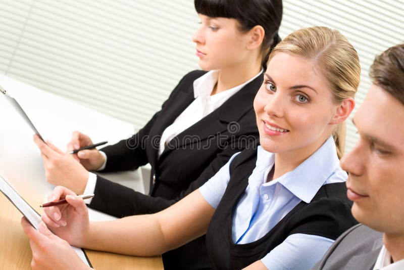 Photo of business lady holding papers and looking at camera among her partners. Photo of business lady holding papers and looking at camera among her partners