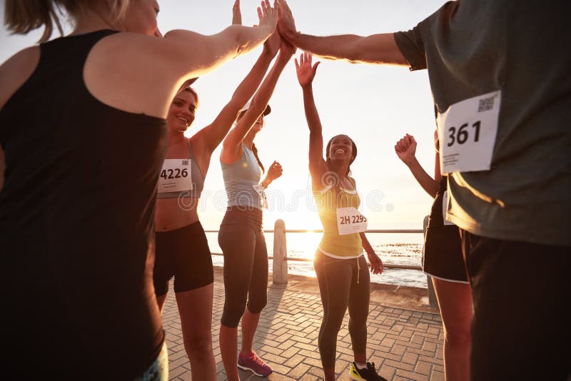 Fit young women with running club group stretching after a run. Young people going stretching workout after a morning run under a city bridge. Fit young women with running club group stretching after a run. Young people going stretching workout after a morning run under a city bridge.