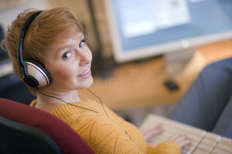 Young smiling woman listening to headphones at computer. Young smiling woman listening to headphones at computer