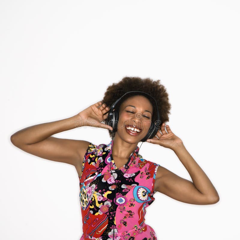 Woman with afro wearing vintage print fabric and listening to headphones smiling and dancing. Woman with afro wearing vintage print fabric and listening to headphones smiling and dancing.