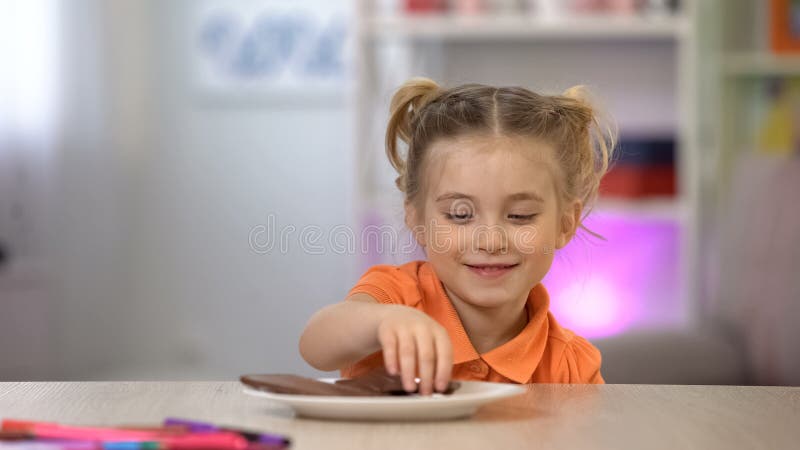 Vrouwelijk jong geitje die in het geheim chocolade van witte plaat op lijst, suikeroverdosis nemen stock afbeeldingen Vrouwelijk jong geitje die in het geheim chocolade van witte plaat op lijst, suikeroverdosis nemen stock afbeeldingen