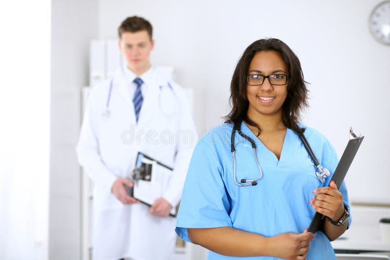 Vrouwelijke Afrikaanse Amerikaanse medische arts met collega's op achtergrond bij het ziekenhuis Geneeskunde en gezondheidszorgco stock foto Vrouwelijke Afrikaanse Amerikaanse medische arts met collega's op achtergrond bij het ziekenhuis Geneeskunde en gezondheidszorgco stock foto
