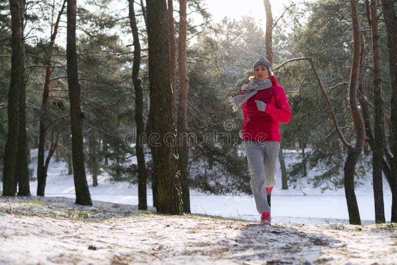 Vrouwelijke agent die in koud de winterbos aanstoot dat warme sportieve lopende kleding en handschoenen draagt royalty-vrije stock afbeelding Vrouwelijke agent die in koud de winterbos aanstoot dat warme sportieve lopende kleding en handschoenen draagt royalty-vrije stock afbeelding