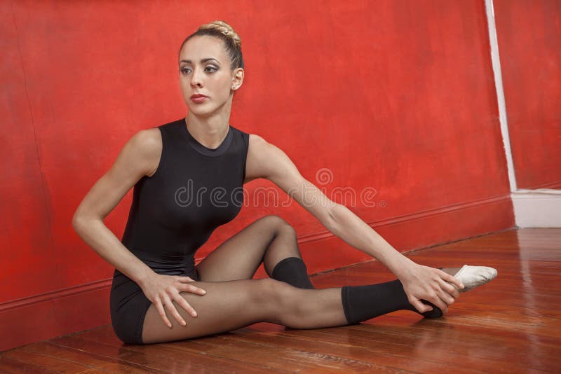 Full length of young female ballet dancer stretching on the floor in dance studio. Full length of young female ballet dancer stretching on the floor in dance studio