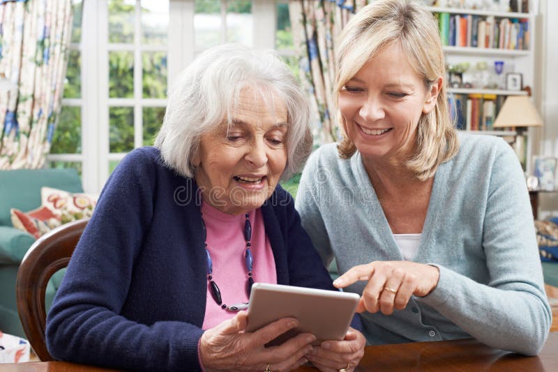 Vrouwelijke Buur die Hogere Vrouw tonen hoe te om Digitale Tablet te gebruiken royalty-vrije stock afbeeldingen Vrouwelijke Buur die Hogere Vrouw tonen hoe te om Digitale Tablet te gebruiken royalty-vrije stock afbeeldingen