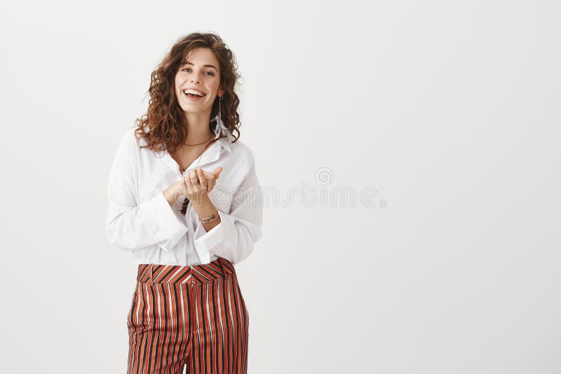 Female colleague clapping hands, applauding friend who achieved success. Portrait of happy carefree woman with curly hair in fashionable clothes, holding palms together over chest and smiling broadly. Female colleague clapping hands, applauding friend who achieved success. Portrait of happy carefree woman with curly hair in fashionable clothes, holding palms together over chest and smiling broadly.