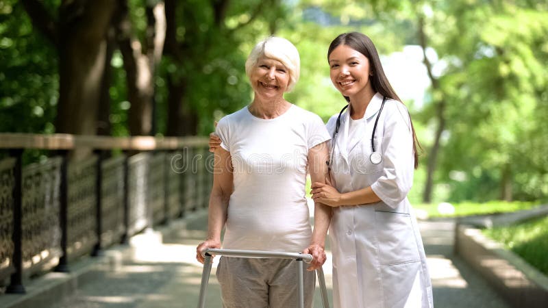 Female doctor hugging old lady with walking frame and smiling at camera outdoors, stock photo. Female doctor hugging old lady with walking frame and smiling at camera outdoors, stock photo