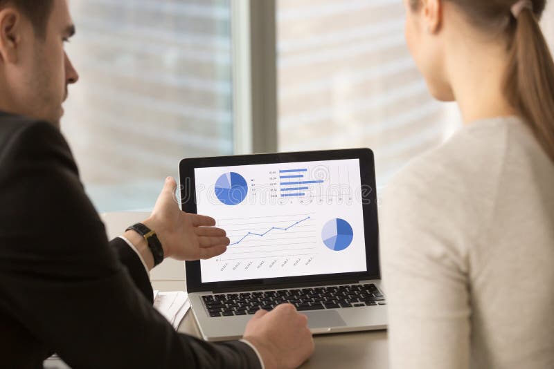 Businessman showing company financial indicators, economic forecast, profitability fluctuations, stats infographics to female colleague or partner on laptop screen at business negotiations. Back view. Businessman showing company financial indicators, economic forecast, profitability fluctuations, stats infographics to female colleague or partner on laptop screen at business negotiations. Back view