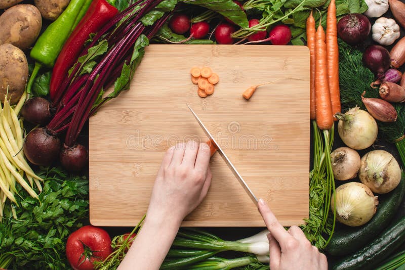 Vrouwelijke Handen met Chef-kok Knife Cutting Carrot op Houten Raad stock fotografie Vrouwelijke Handen met Chef-kok Knife Cutting Carrot op Houten Raad stock fotografie