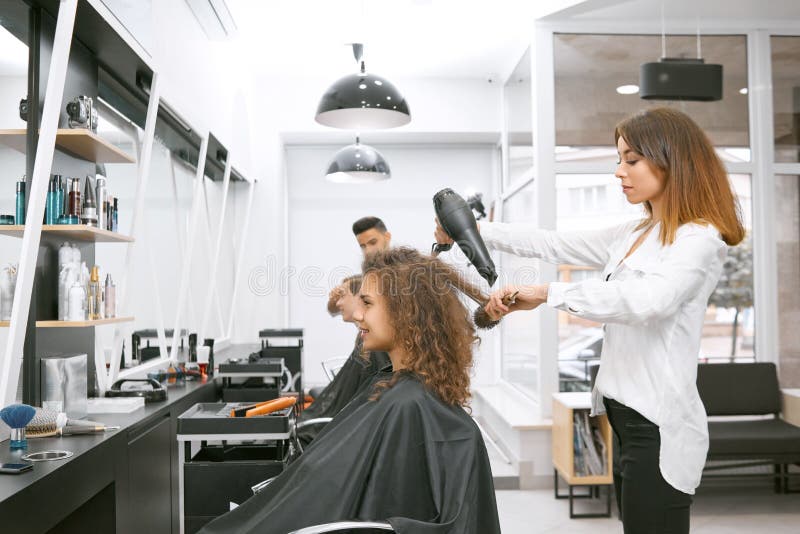 Vrouwelijke herenkapper die krullend meisjes` s haar drogen die grote plastic borstel gebruiken stock foto's Vrouwelijke herenkapper die krullend meisjes` s haar drogen die grote plastic borstel gebruiken stock foto's