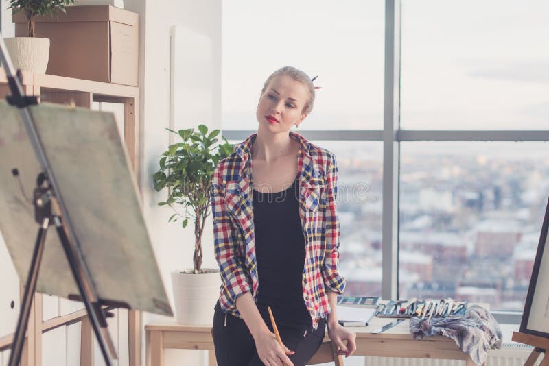 Vrouwelijke schilder die zich in workshop bevinden, lettend op bij aandachtig tekening die, penseel houden Kunstenaar die op beel royalty-vrije stock foto Vrouwelijke schilder die zich in workshop bevinden, lettend op bij aandachtig tekening die, penseel houden Kunstenaar die op beel royalty-vrije stock foto