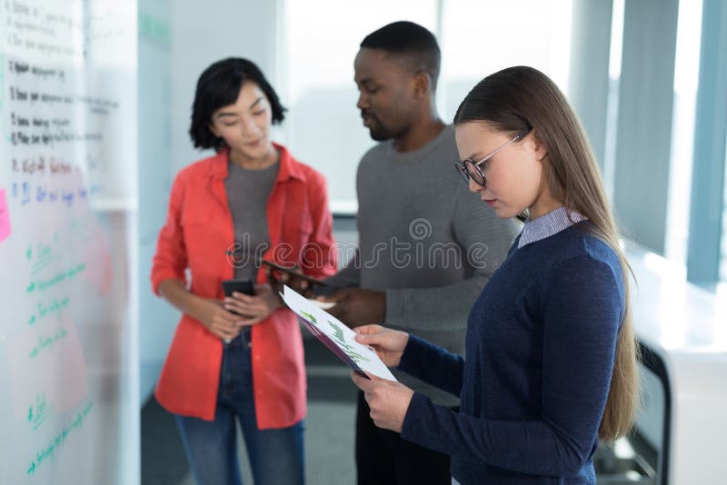 Vrouwelijke stafmedewerker die grafiek met collega's op achtergrond bekijken royalty-vrije stock afbeelding Vrouwelijke stafmedewerker die grafiek met collega's op achtergrond bekijken royalty-vrije stock afbeelding