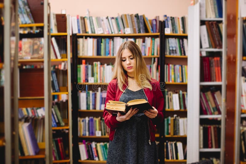 Vrouwelijke student die een boek tussen boekenrekken in universitaire bibliotheek lezen royalty-vrije stock fotografie Vrouwelijke student die een boek tussen boekenrekken in universitaire bibliotheek lezen royalty-vrije stock fotografie