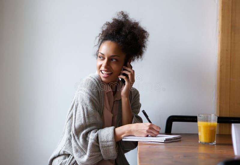 Vrouwelijke student die thuis en op mobiele telefoon spreken werken stock afbeelding Vrouwelijke student die thuis en op mobiele telefoon spreken werken stock afbeelding