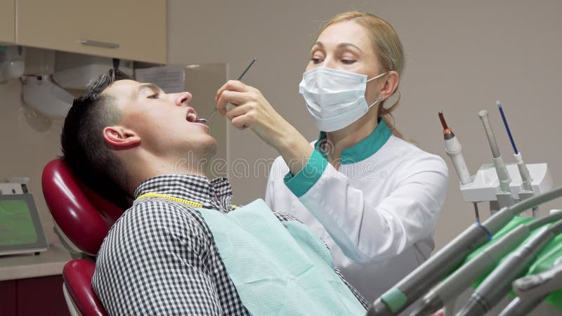 Vrouwelijke tandarts die tanden die van haar patiënt onderzoeken, bij tandkliniek werken