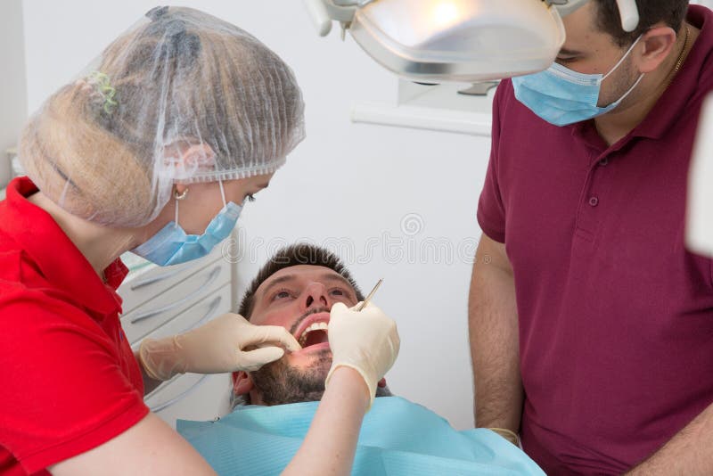 Vrouwelijke Tandarts met mannelijke medewerker die mensen geduldige tanden onderzoeken bij medische kliniek royalty-vrije stock afbeelding Vrouwelijke Tandarts met mannelijke medewerker die mensen geduldige tanden onderzoeken bij medische kliniek royalty-vrije stock afbeelding
