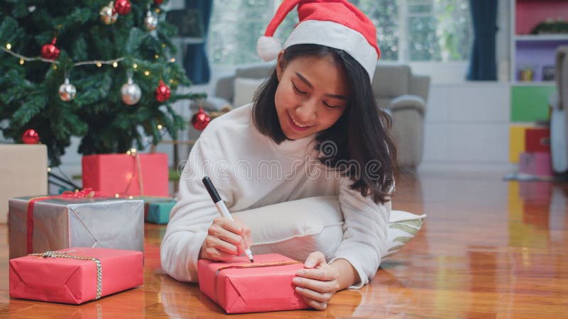 Vrouwelijke tieners dragen sweater en santa die ontspannen en blij zijn met het schrijven van een cadeautje bij kerstboom, geniet stock afbeelding Vrouwelijke tieners dragen sweater en santa die ontspannen en blij zijn met het schrijven van een cadeautje bij kerstboom, geniet stock afbeelding