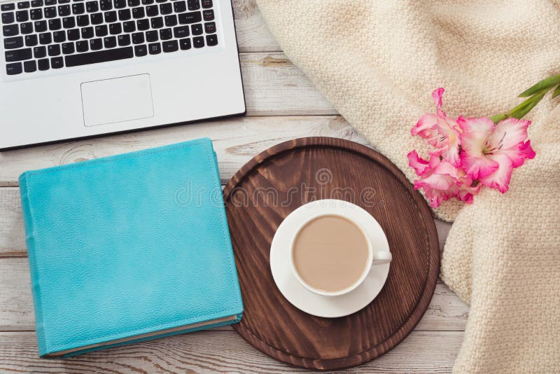 Vrouwelijke werkplaats met laptop, kop van koffie, blauw notitieboekje, comfortabele sweater en roze bloemen op houten achtergron royalty-vrije stock foto Vrouwelijke werkplaats met laptop, kop van koffie, blauw notitieboekje, comfortabele sweater en roze bloemen op houten achtergron royalty-vrije stock foto