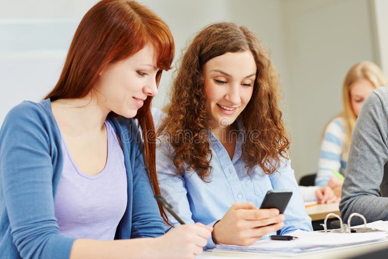 Two young women looking at their smartphone in university class. Two young women looking at their smartphone in university class