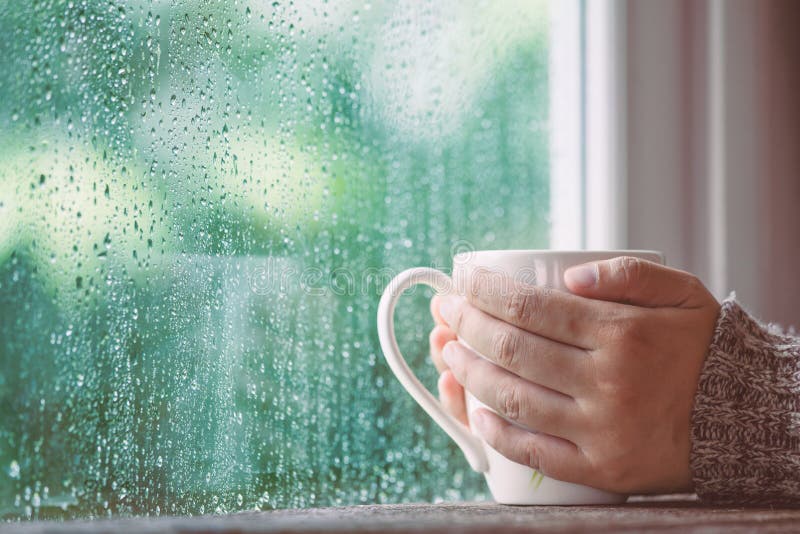 Vrouwenhand die de kop van koffie of thee op regenachtig dagvenster houden