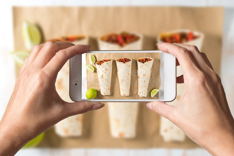 Vrouwenhanden die een foto van smakelijke eigengemaakte burrito met groenten en rundvlees op een document nemen royalty-vrije stock foto's Vrouwenhanden die een foto van smakelijke eigengemaakte burrito met groenten en rundvlees op een document nemen royalty-vrije stock foto's