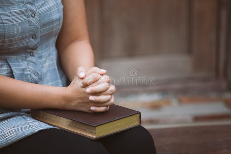 Vrouwenhanden in gebed op een Heilige Bijbel voor geloofsconcept dat worden gevouwen