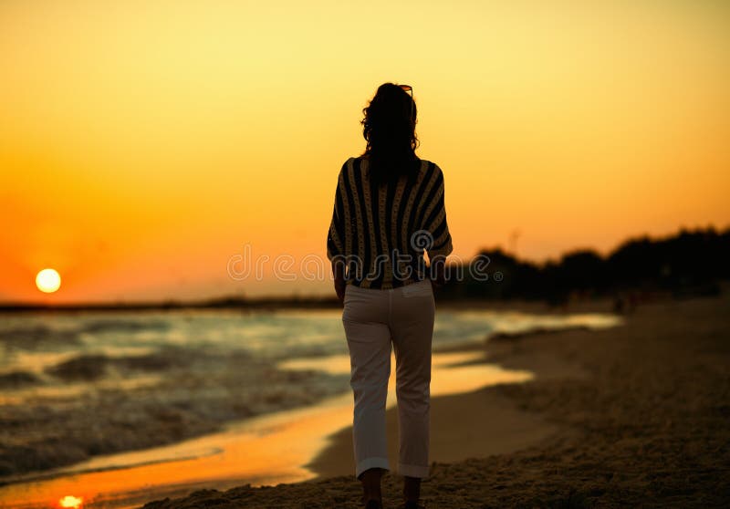 Vu par derrière la femme élégante sur la plage dans la marche de soirée images stock Vu par derrière la femme élégante sur la plage dans la marche de soirée images stock