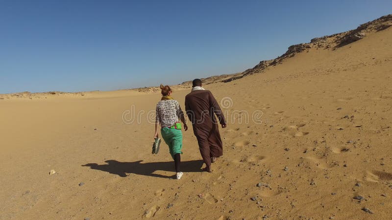 Vue arrière d'homme nubian marchant dans le désert avec le touriste féminin banque de vidéos