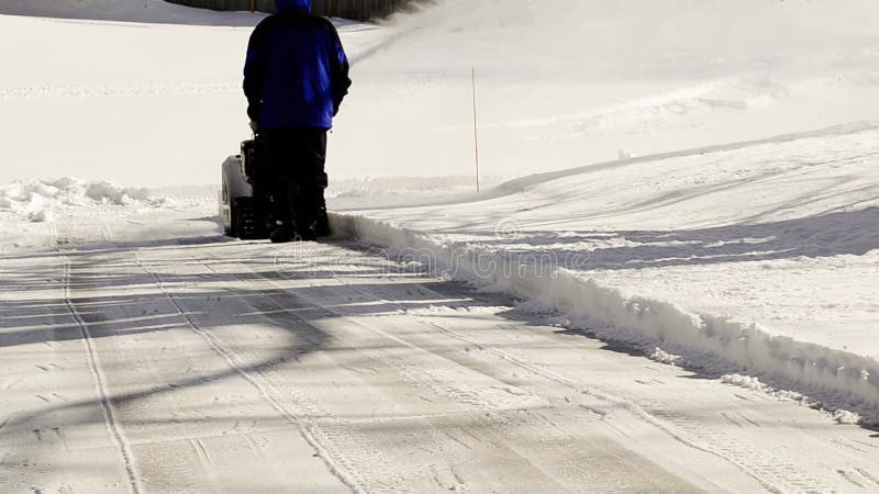 Vue arrière d'un homme déneigeant une allée résidentielle après une forte chute de neige banque de vidéos