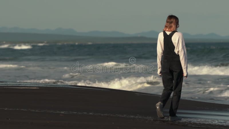 Vue arrière d'un modèle méconnaissable marchant sur la plage de sable sur fond de vagues de rupture de l'océan banque de vidéos
