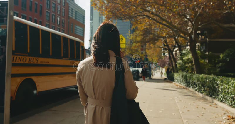 Vue arrière d'une brune élégante en flânant dans les rues ensoleillées de new york city en passant par un arrêt de bus scolaire banque de vidéos