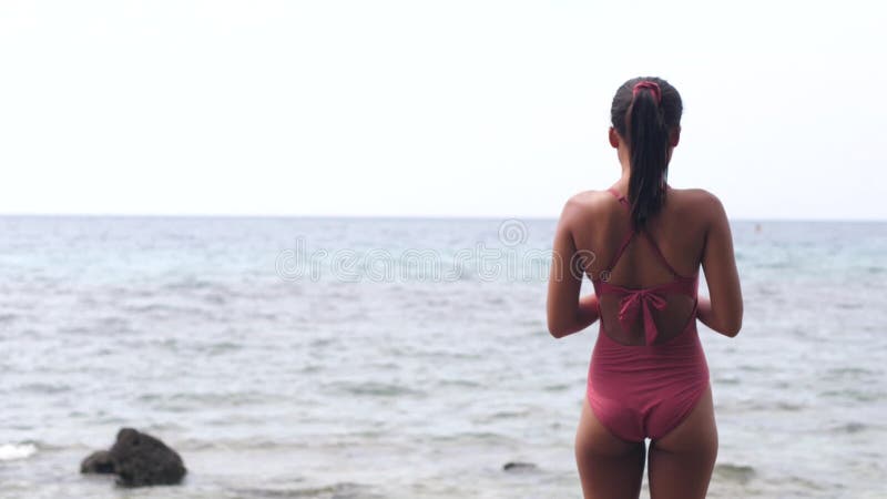 Vue arrière d'une femme mineure en maillot de bain rose devant l'océan clips vidéos