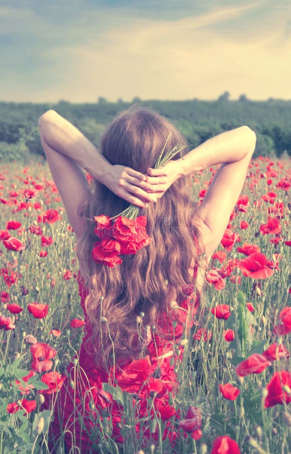 Vue arrière d'une jeune femme avec de longs cheveux blonds dans une robe rouge tenant un bouquet des fleurs dans un domaine de pa photographie stock Vue arrière d'une jeune femme avec de longs cheveux blonds dans une robe rouge tenant un bouquet des fleurs dans un domaine de pa photographie stock