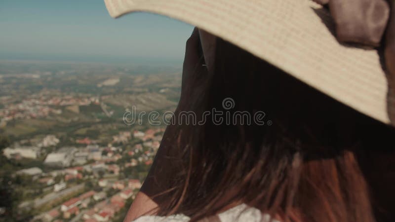 Vue arrière d'une jolie toriste féminine dans un chapeau de paille prenant des photos de vues époustouflantes de san marino avec c banque de vidéos