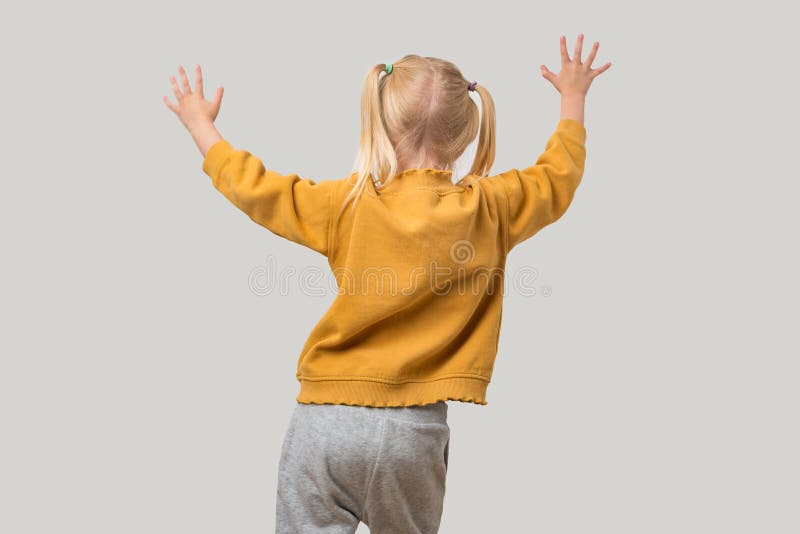 Vue arrière d'une petite fille dans un hoodie jaune debout et levant ses mains isolées sur fond gris image stock