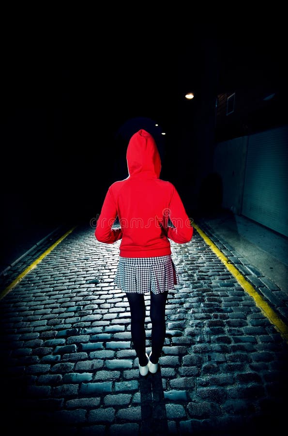 Full length rear view of a woman in red hood jacket standing on cobbled street at night. Full length rear view of a woman in red hood jacket standing on cobbled street at night