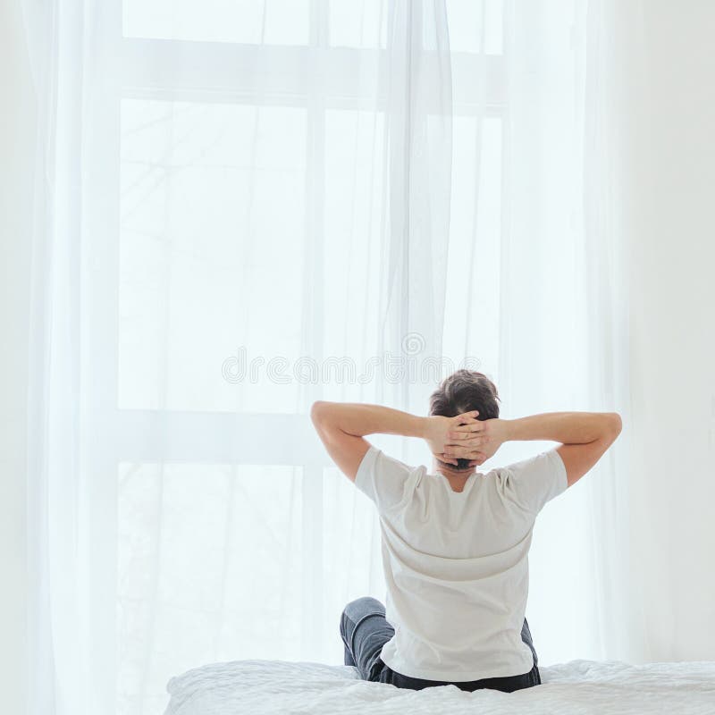 Vue arrière de jeune homme se reposant sur le lit pendant le matin et tenant des mains derrière la tête photos stock Vue arrière de jeune homme se reposant sur le lit pendant le matin et tenant des mains derrière la tête photos stock