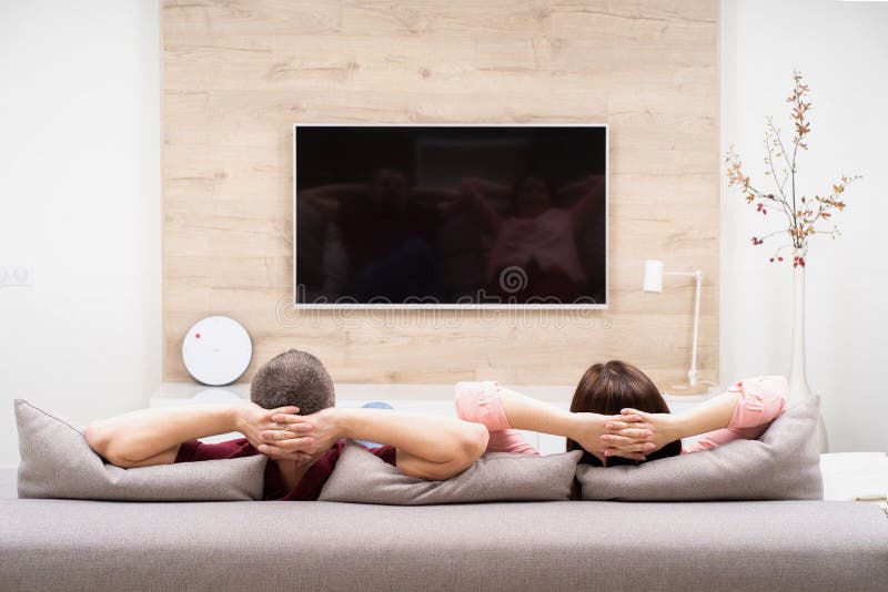 Vue arrière de l'homme et de la femme de couples se reposant en appartement, se reposant au sofa ensemble et à la TV de observati images libres de droits Vue arrière de l'homme et de la femme de couples se reposant en appartement, se reposant au sofa ensemble et à la TV de observati images libres de droits