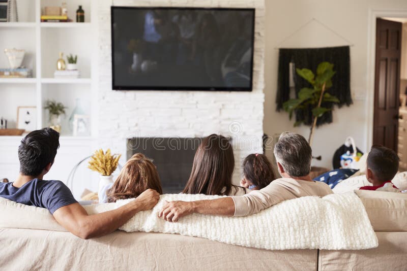 Vue arrière de la famille hispanique de trois générations se reposant sur le sofa regardant la TV image stock