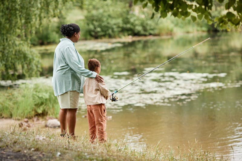 Vue arrière de la mère et de la fille pêchant ensemble par lac image libre de droits