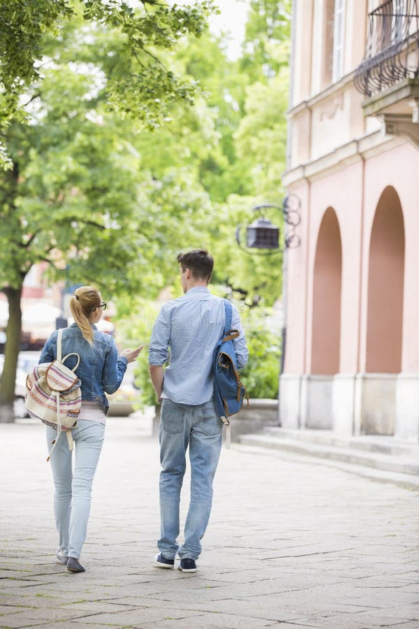 Full length rear view of young college friends talking while walking in campus. Full length rear view of young college friends talking while walking in campus