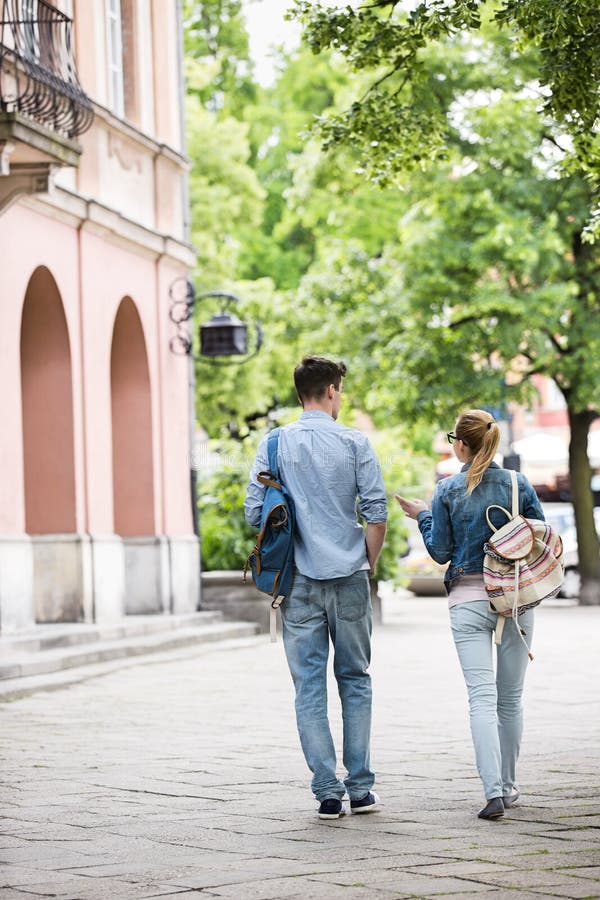 Full length rear view of young college friends talking while walking in campus. Full length rear view of young college friends talking while walking in campus