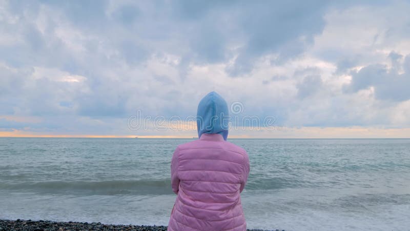 Vue arrière : une femme se tient sur le rivage en regardant les vagues orageuses banque de vidéos