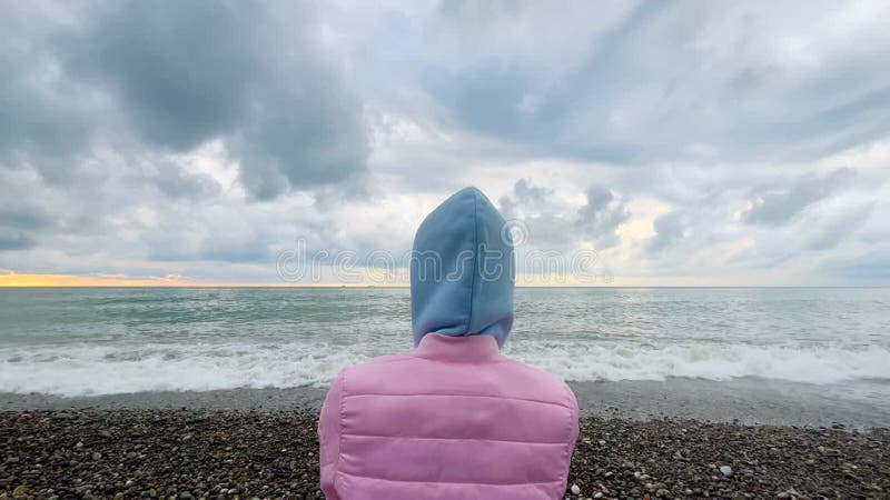 Vue arrière : une femme se tient sur le rivage en regardant les vagues orageuses banque de vidéos
