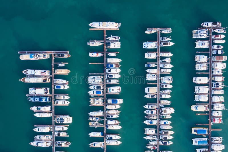 Aerial view of a white motor yacht. Yacht enters the bay in the parking lot. Many different yachts, catamarans moored to piers. Expensive yacht and travel place. Drone shot. Aerial view of a white motor yacht. Yacht enters the bay in the parking lot. Many different yachts, catamarans moored to piers. Expensive yacht and travel place. Drone shot