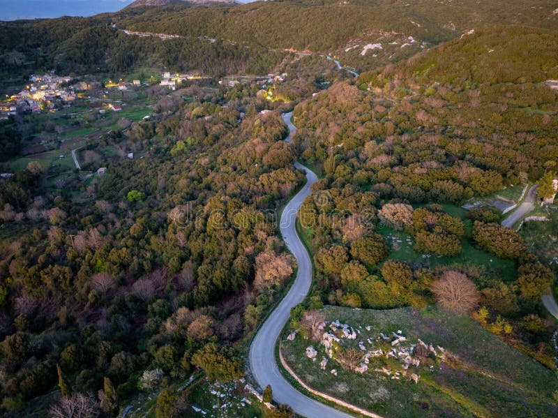 Vue aérienne d'une route sinueuse à travers les collines verdoyantes et le village au coucher du soleil. photo stock