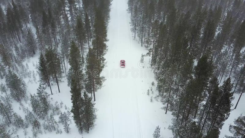Vue aérienne de la seule voiture rouge sur la route dans le beau paysage d'hiver de la Laponie pendant chutes de neige banque de vidéos