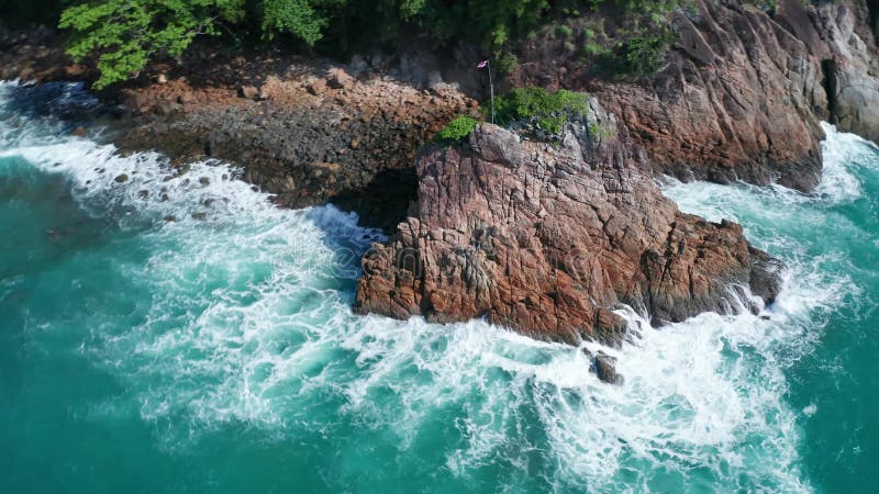 Vue aérienne des belles vagues et de la côte tropicale rocheuse de l'océan avec le drapeau thaïlandais sur la crête de la roche banque de vidéos