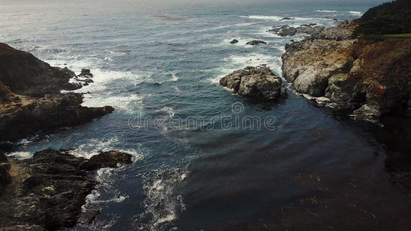 Vue aérienne : Les vagues enroulent dans une enclave cachée le long de la côte de Big Sur. banque de vidéos